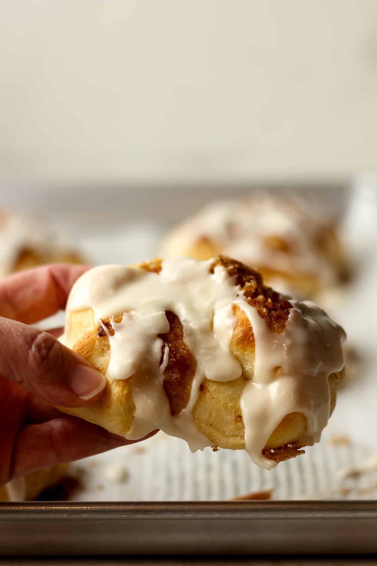 My hand holding a cinnamon roll knot with icing.