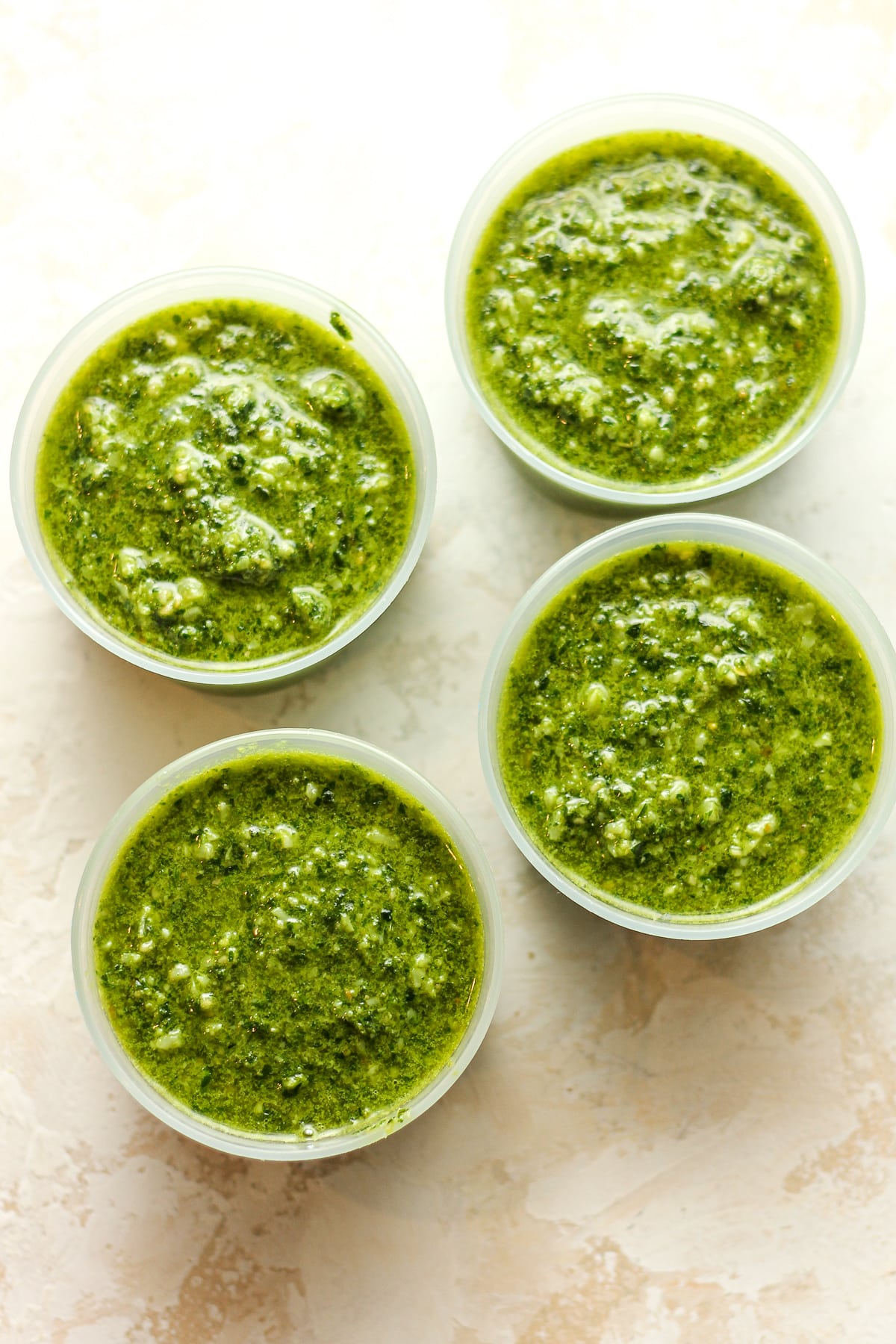 Overhead view of four small containers of pesto with spinach.