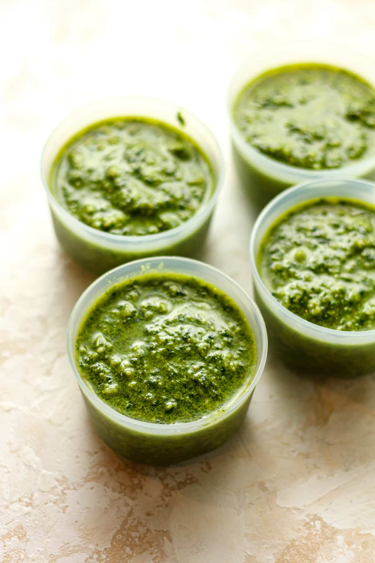 Side view of four small containers of spinach pesto.
