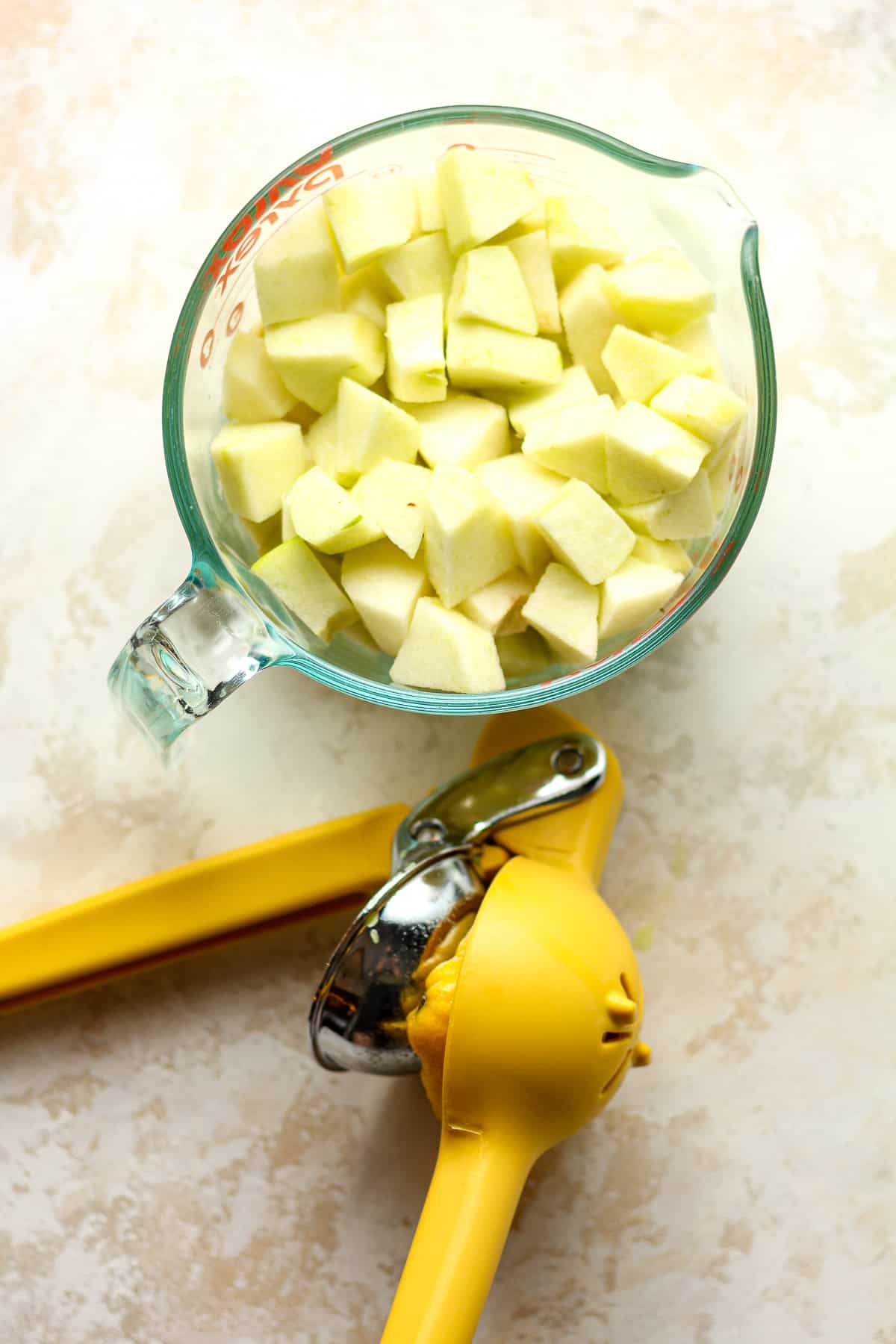 A measuring cup of the cubed apples with a citrus press.