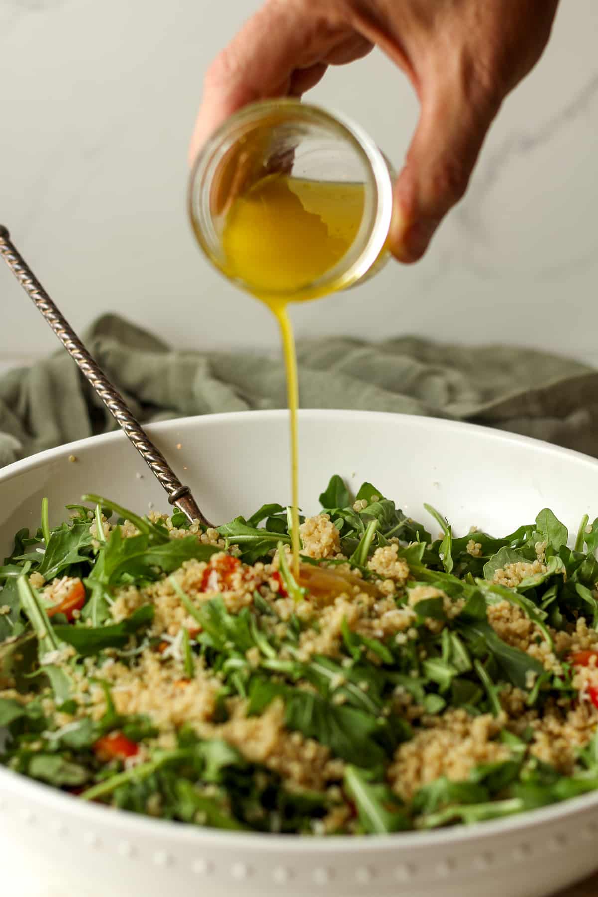 A hand drizzling the salad dressing over the salad.