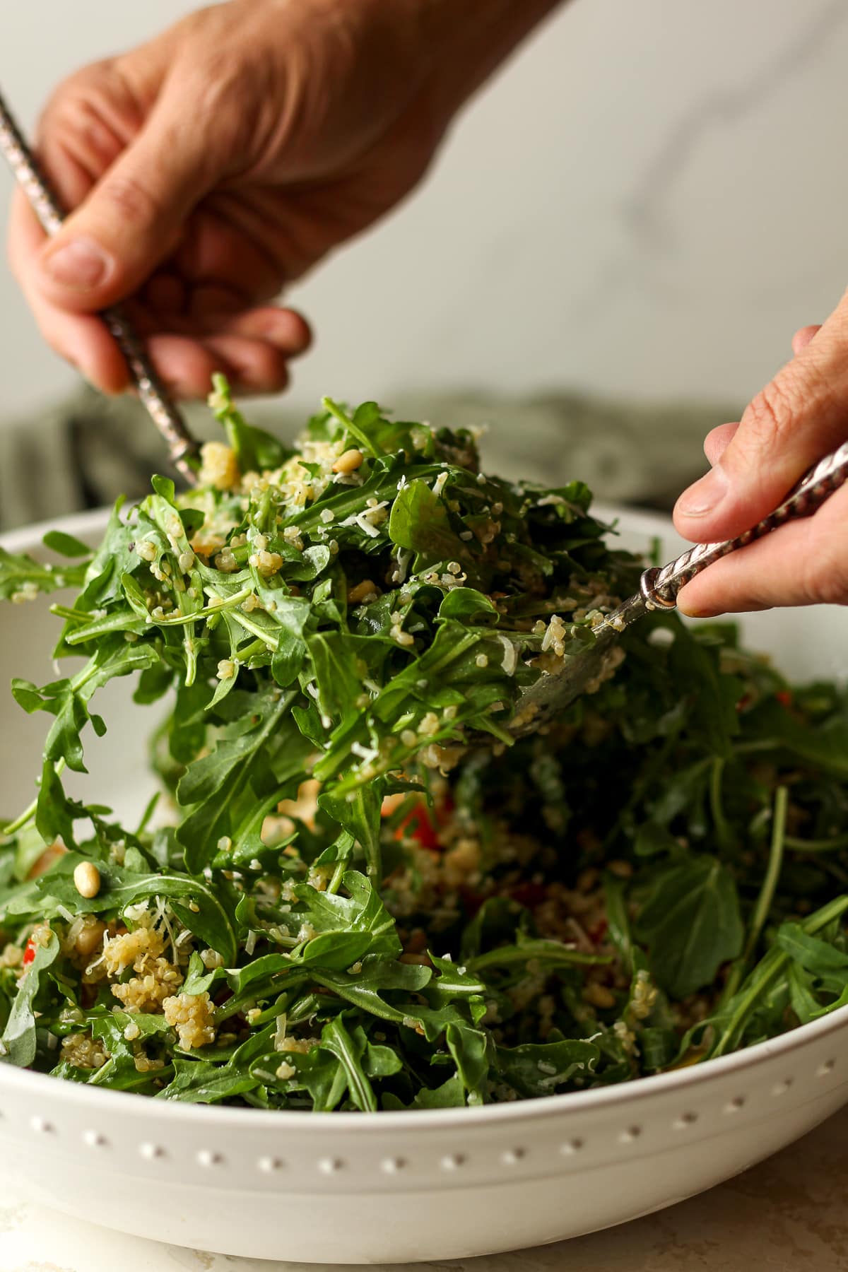 The large salad being tossed by hands.