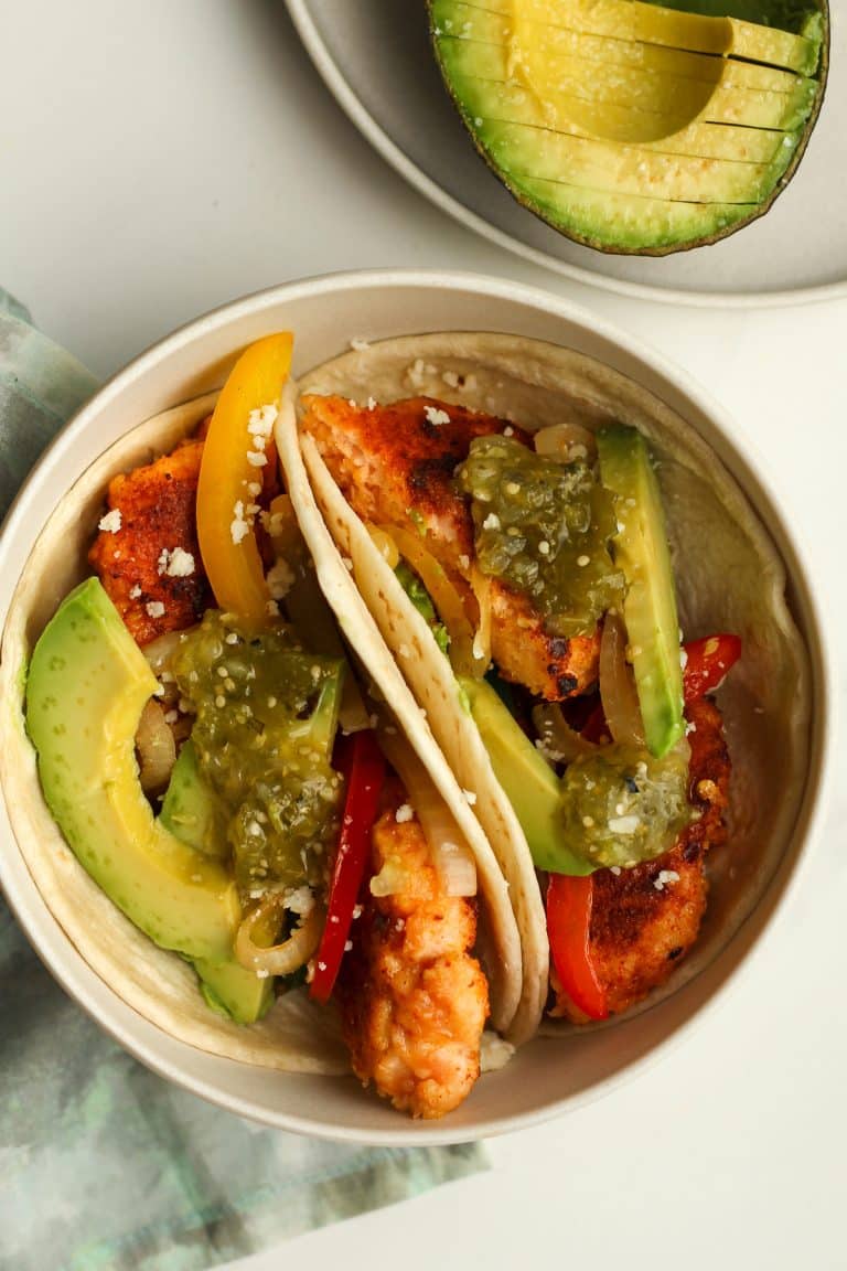 A small bowl with two blackened salmon tacos with avocado.