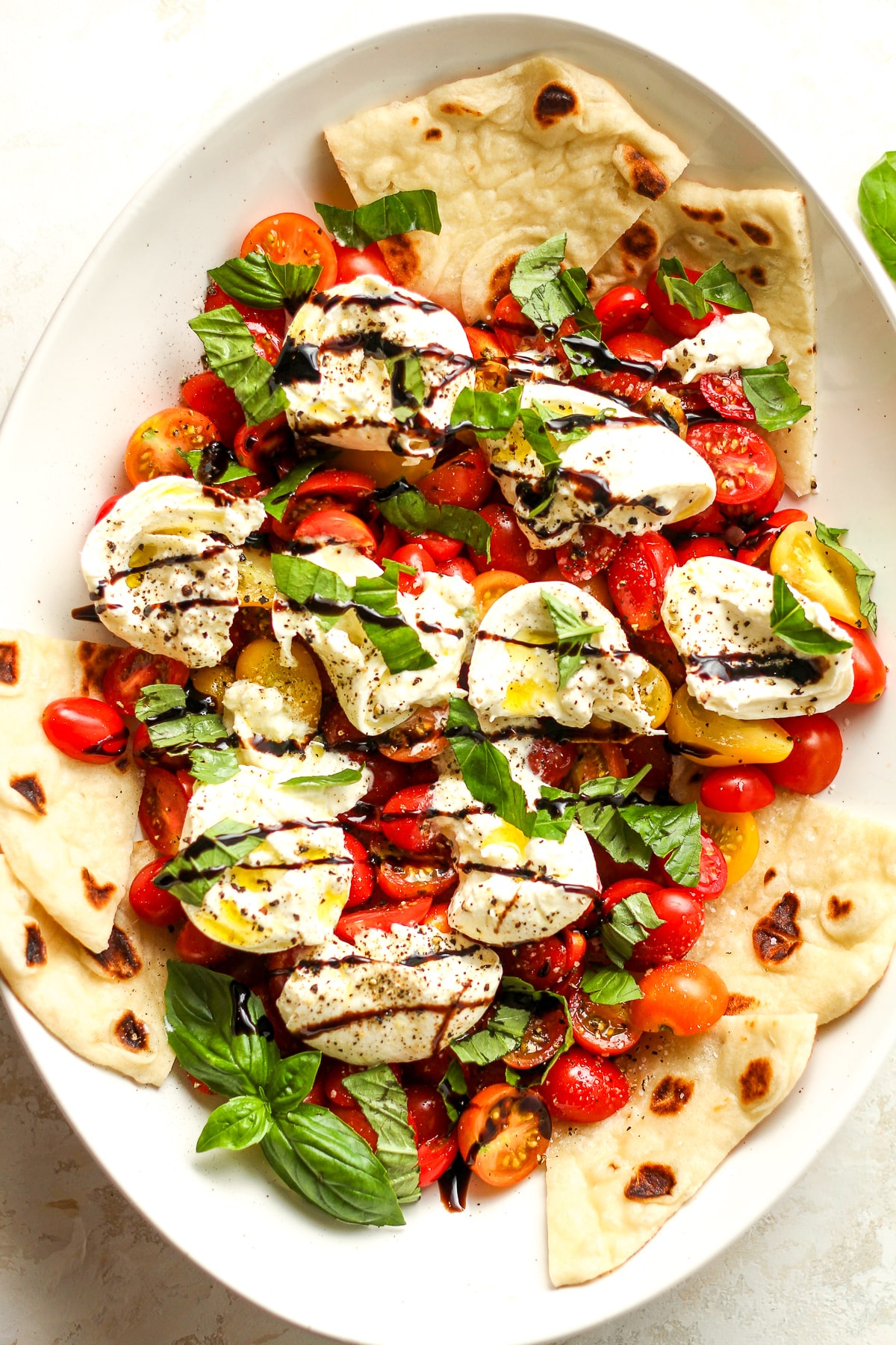 An oblong platter of burrata caprese salad with fresh basil.