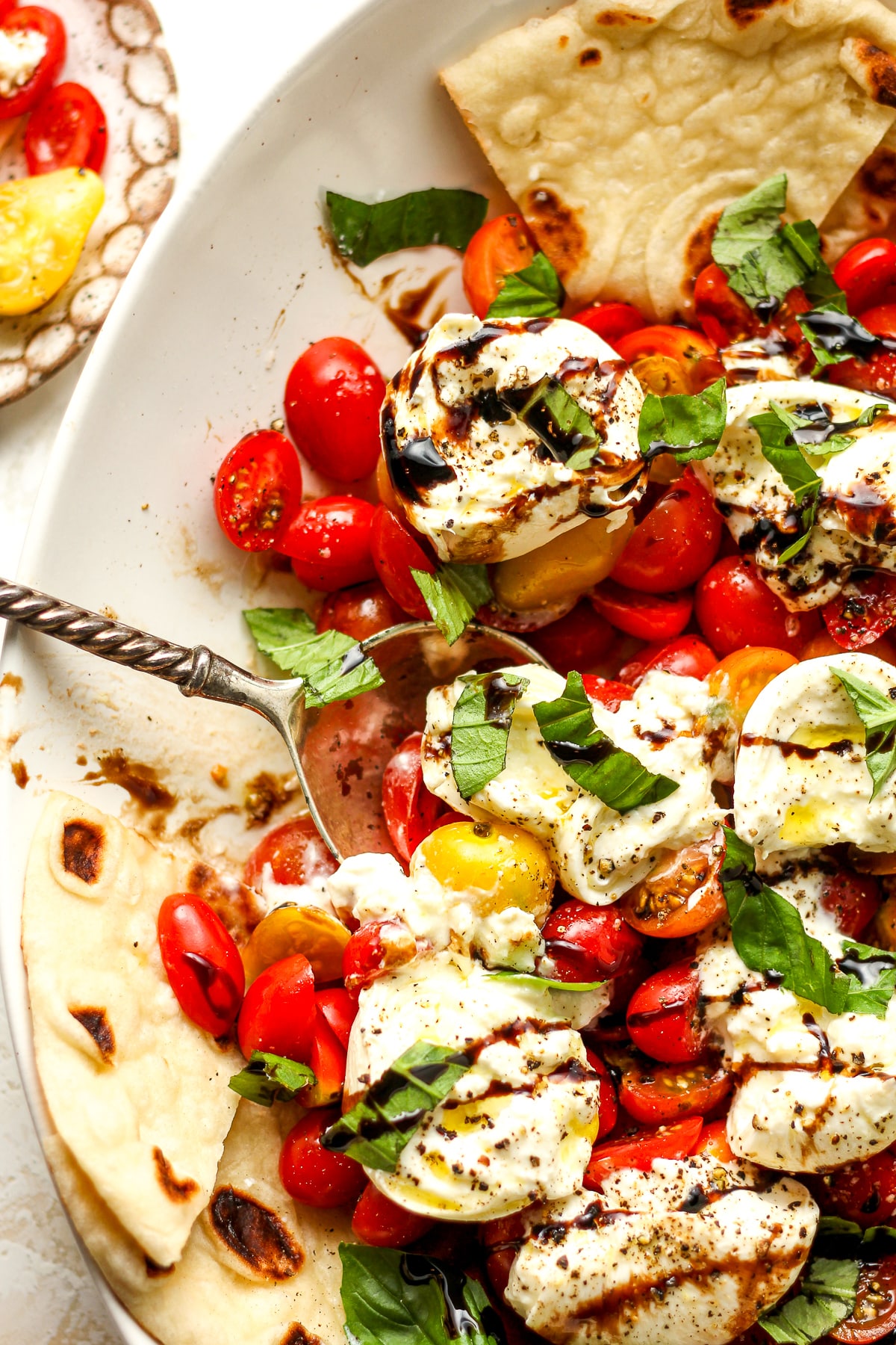 A platter of burrata caprese with a serving spoon.