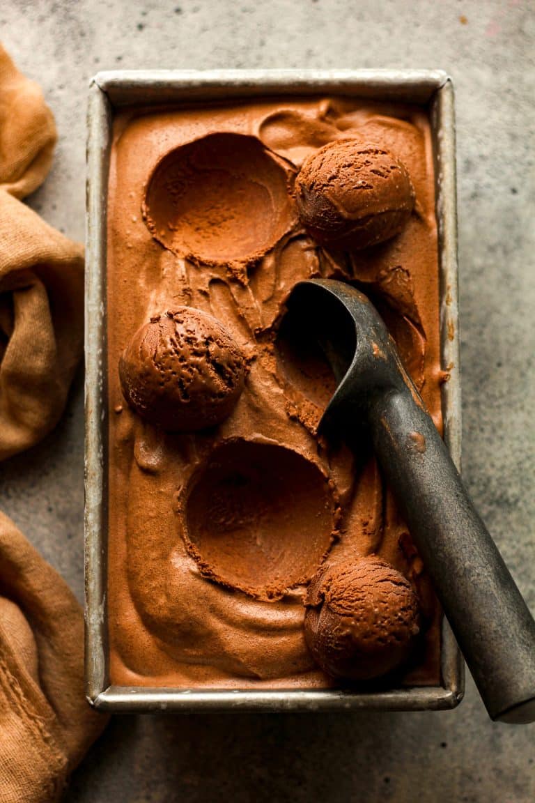 Closeup on a loaf pan of dark chocolate ice cream with several dips out and a scoop.