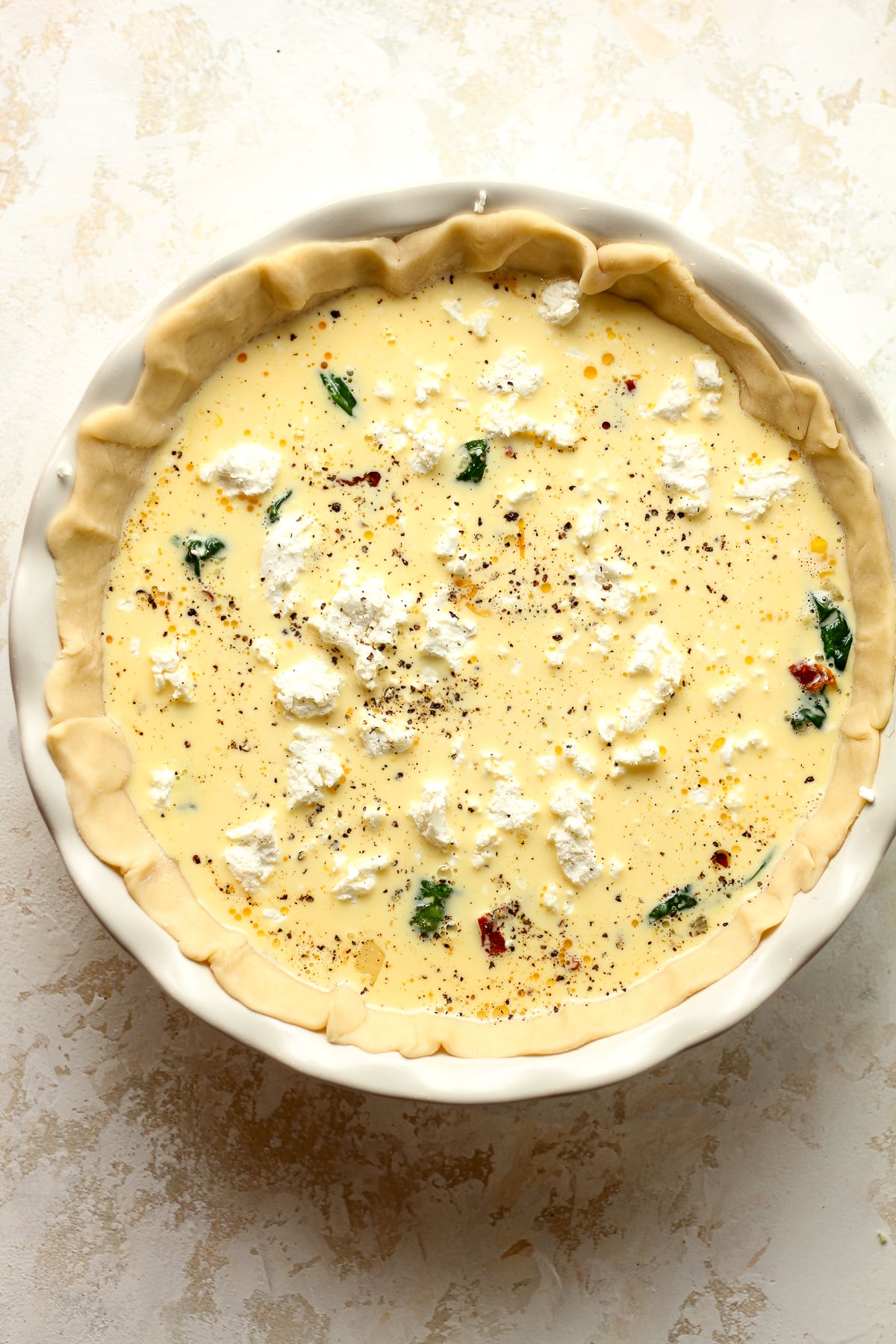 A pie plate with the prepared goat cheese quiche.