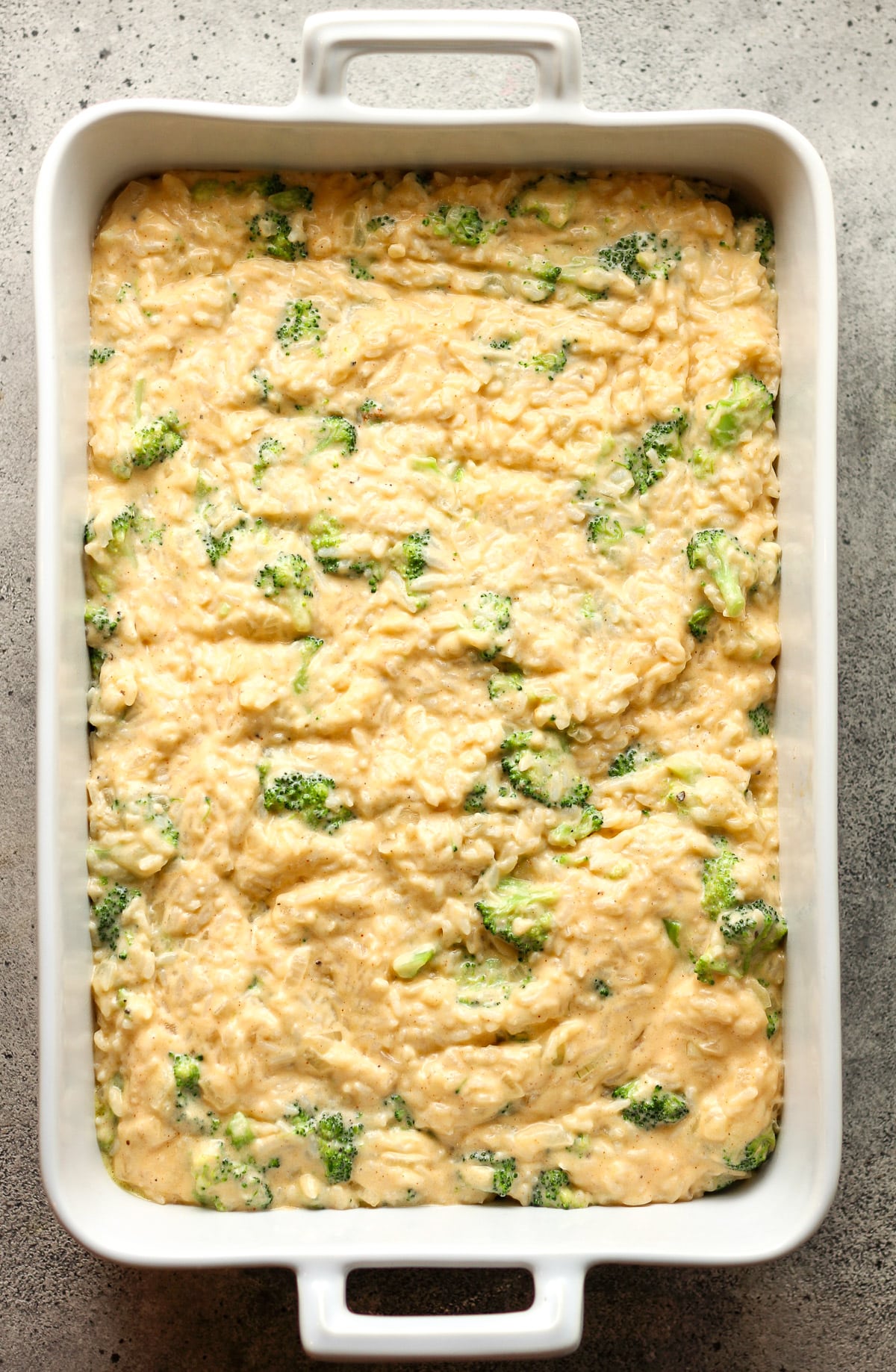 A 9x13 baking dish of the unbaked broccoli rice casserole.