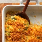 A wooden spoon digging into a broccoli rice casserole with breadcrumb topping.