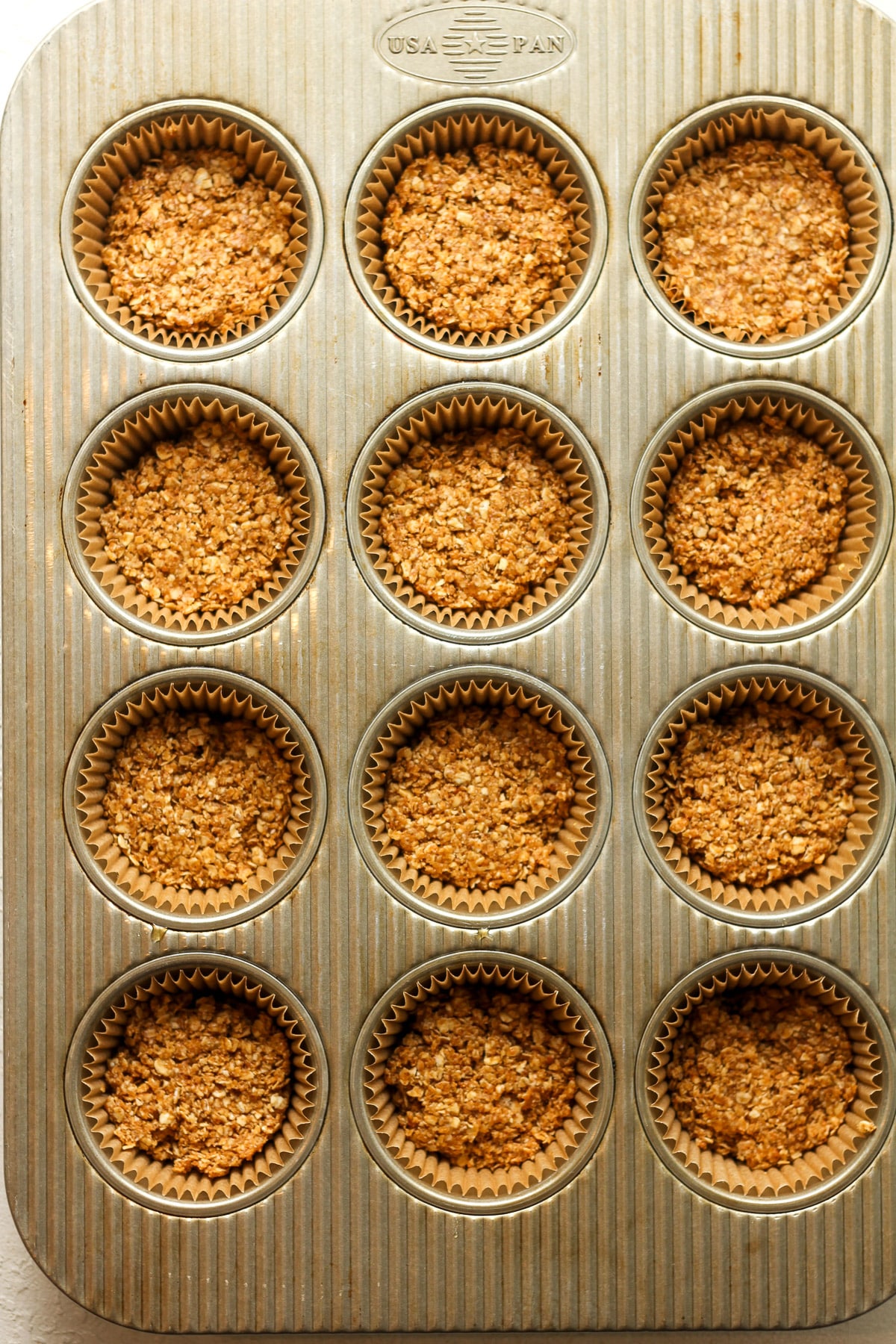 A cupcake pan of some paper liners with peanut butter oatmeal mixture pressed inside.