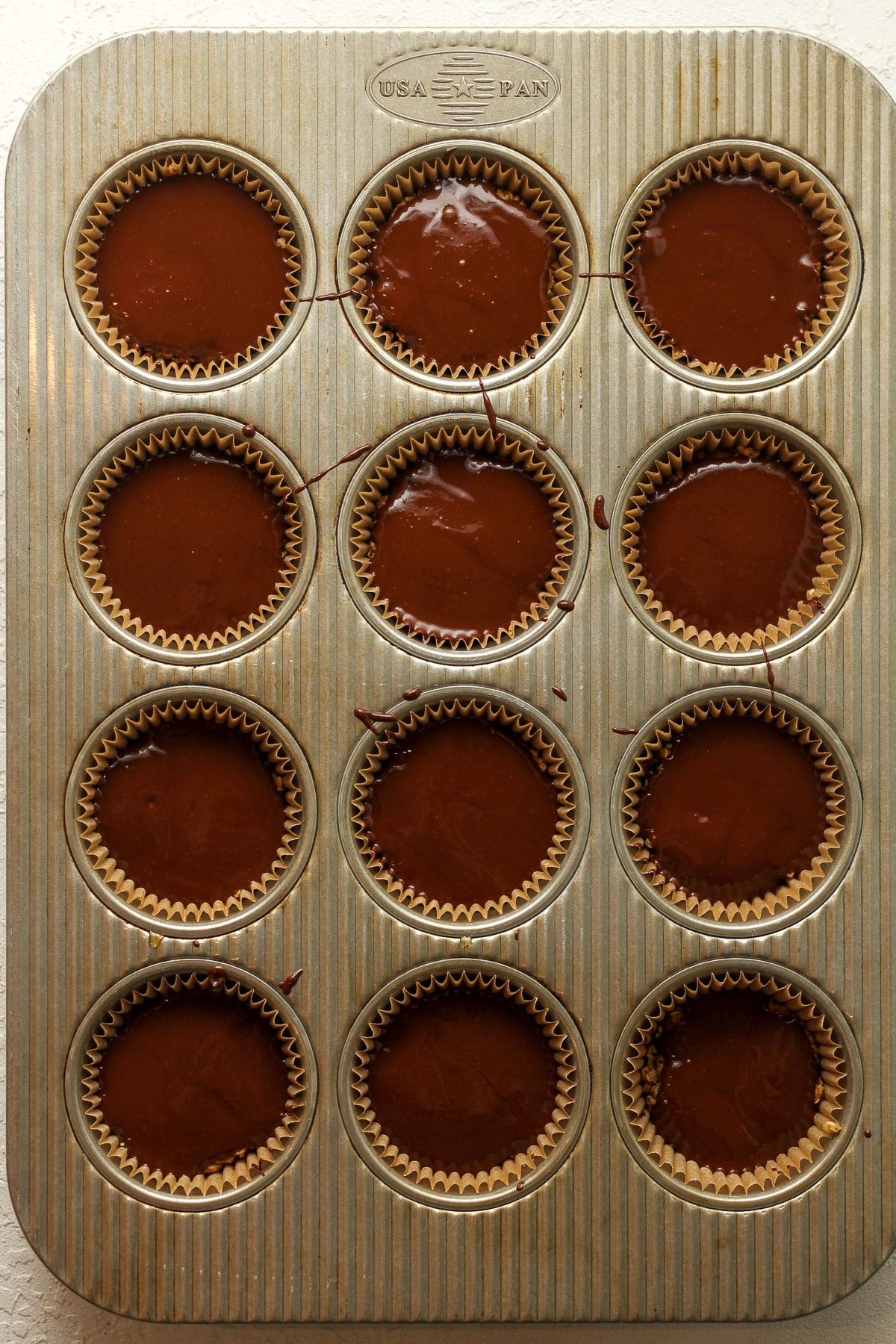 A cupcake pan of the prepped oat cups with melty chocolate on top.