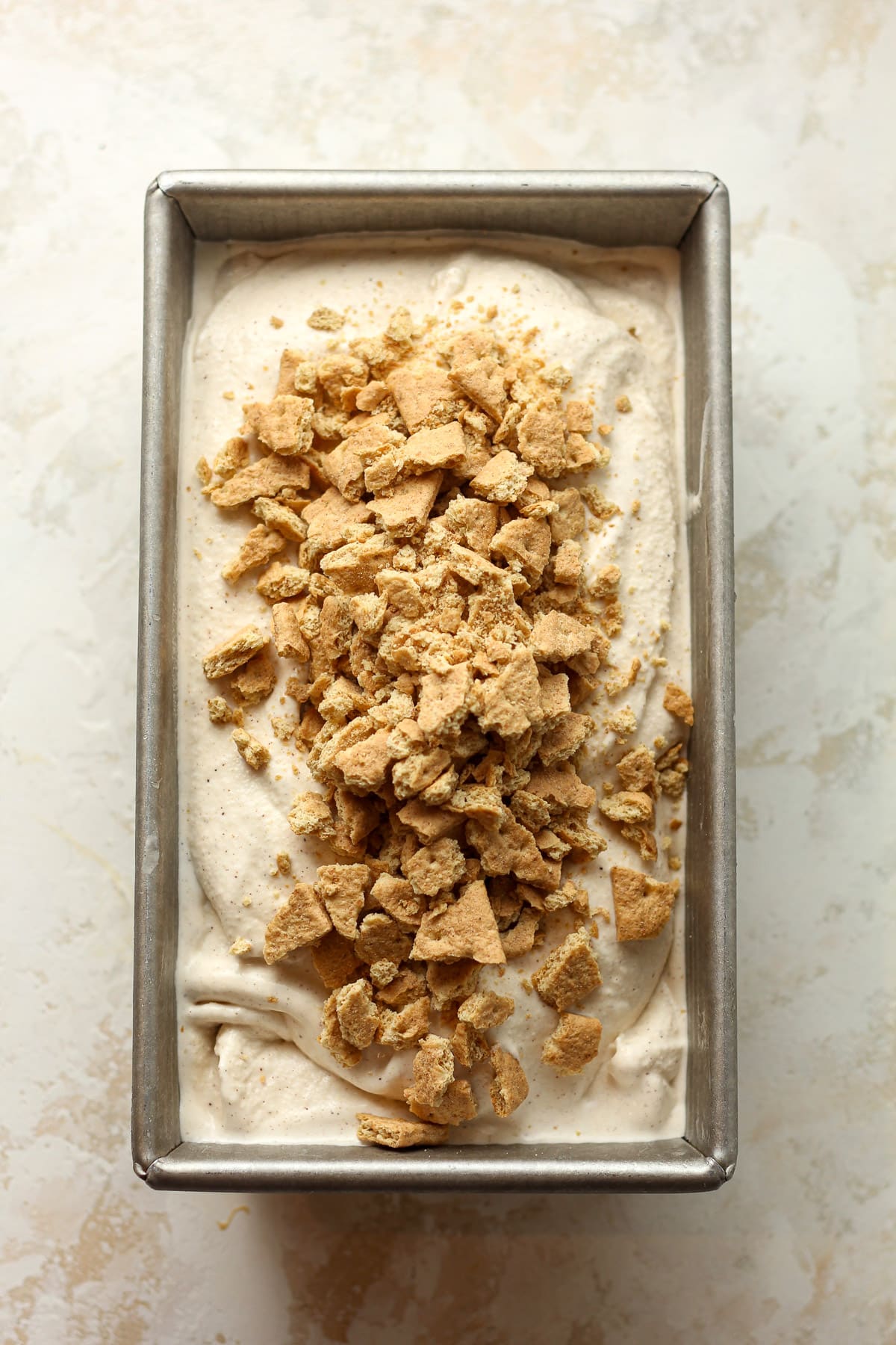 A loaf pan of cinnamon ice cream with graham crackers on top.