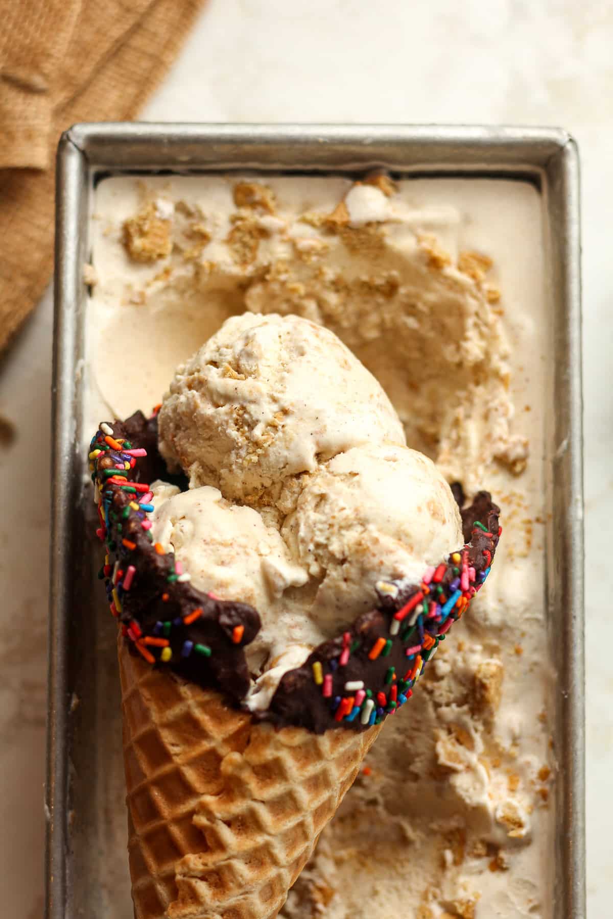 Closeup on a pan of a waffle cone of cinnamon ice cream in a loaf pan of ice cream.