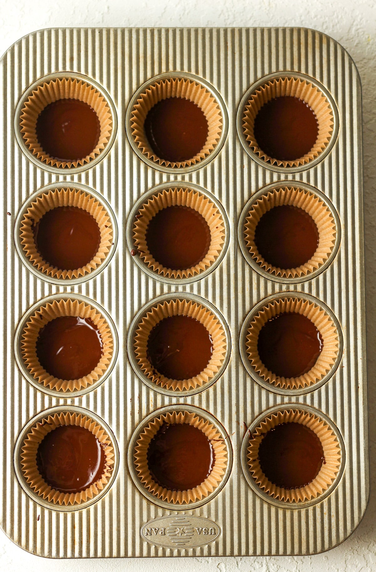 The muffin pan with some chocolate in paper liners.