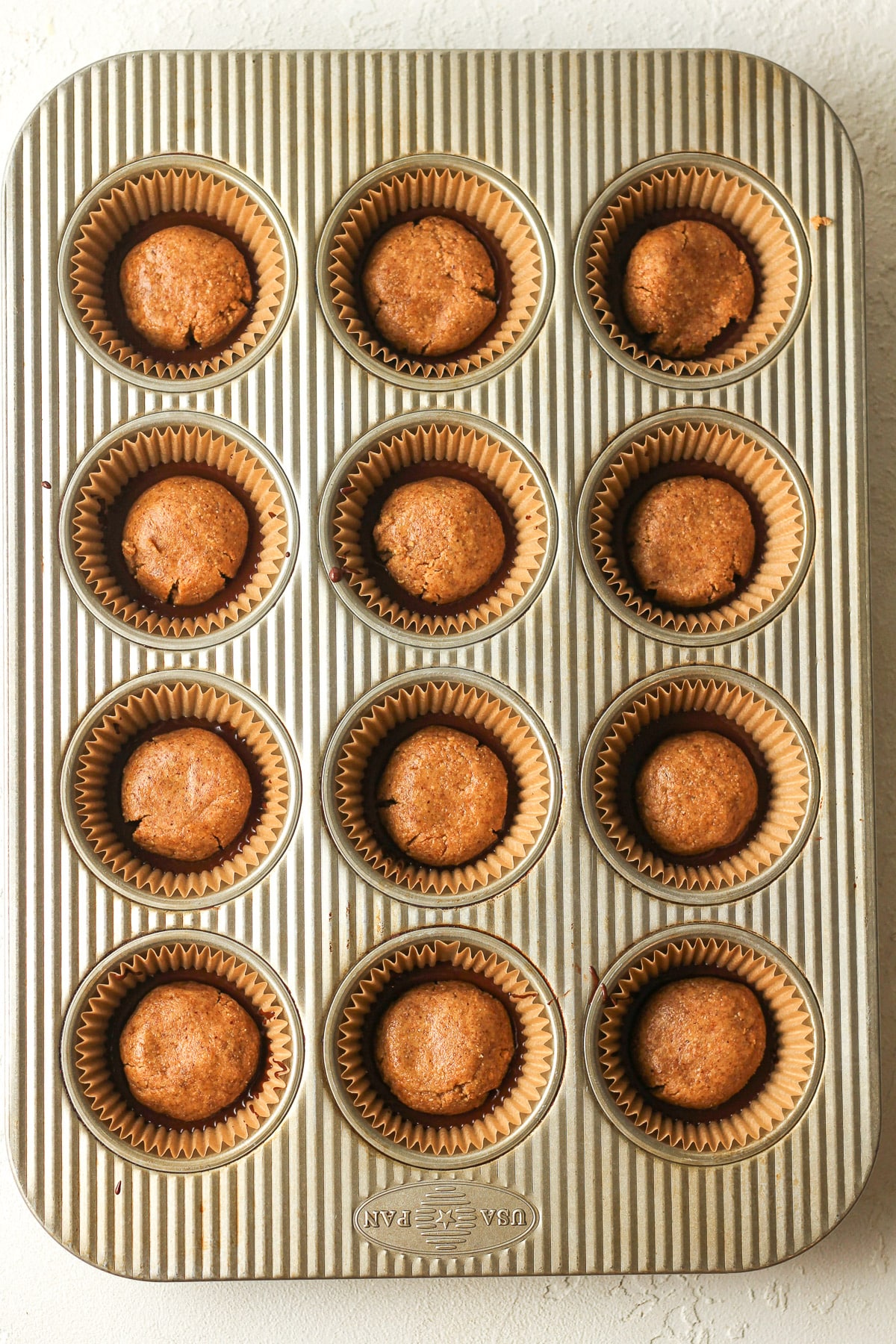 A muffin tin with the peanut rounds on top of the chocolate.