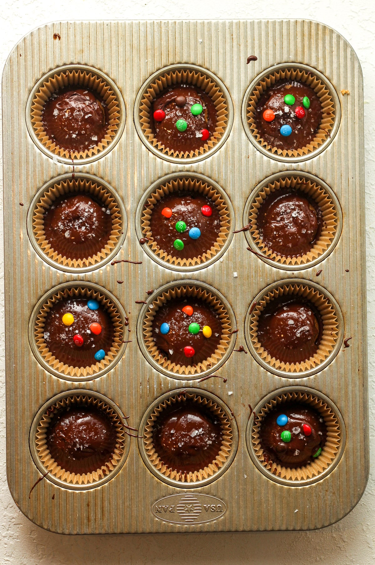 The muffin pan with the melted chocolate on top of the peanut butter rounds.