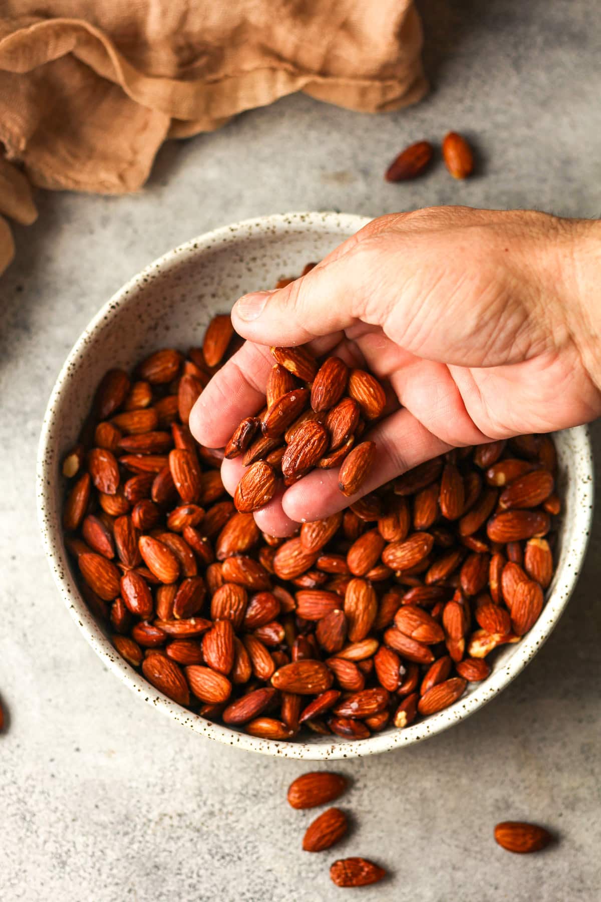 A hand reaching for some smoked almonds out of a bowl.