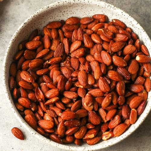 A bowl of smoked almonds on a gray background.