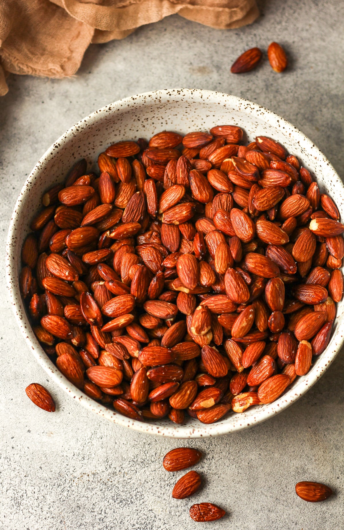 A bowl of smoked almonds on a gray background.