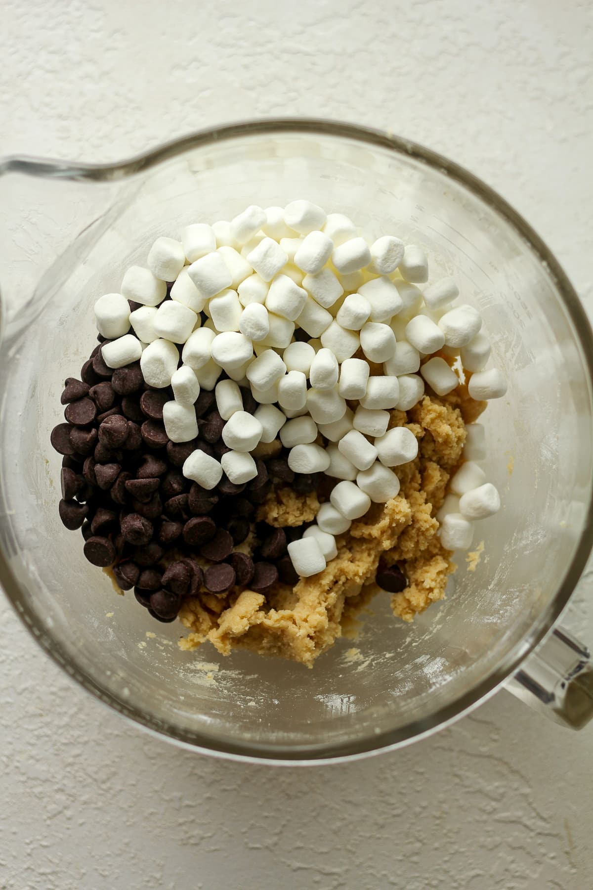 A mixing bowl of the cookie dough with chocolate chips and marshmallows on top.