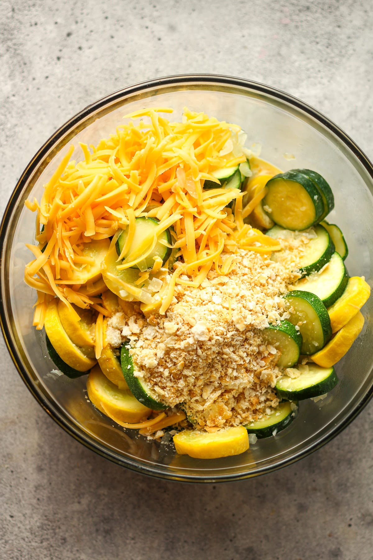 A large glass bowl of the sautéed squash, crackers, cheese, eggs, and half and half.