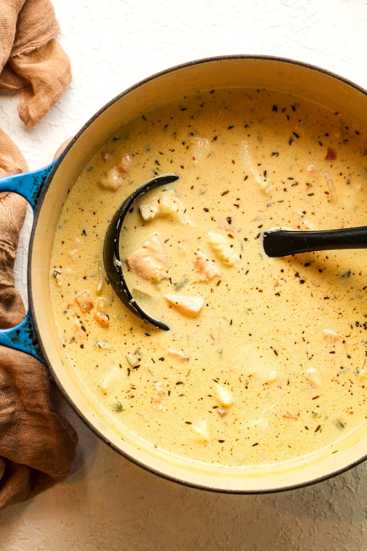 A pot of the finished Irish seafood chowder with a black soup ladle.