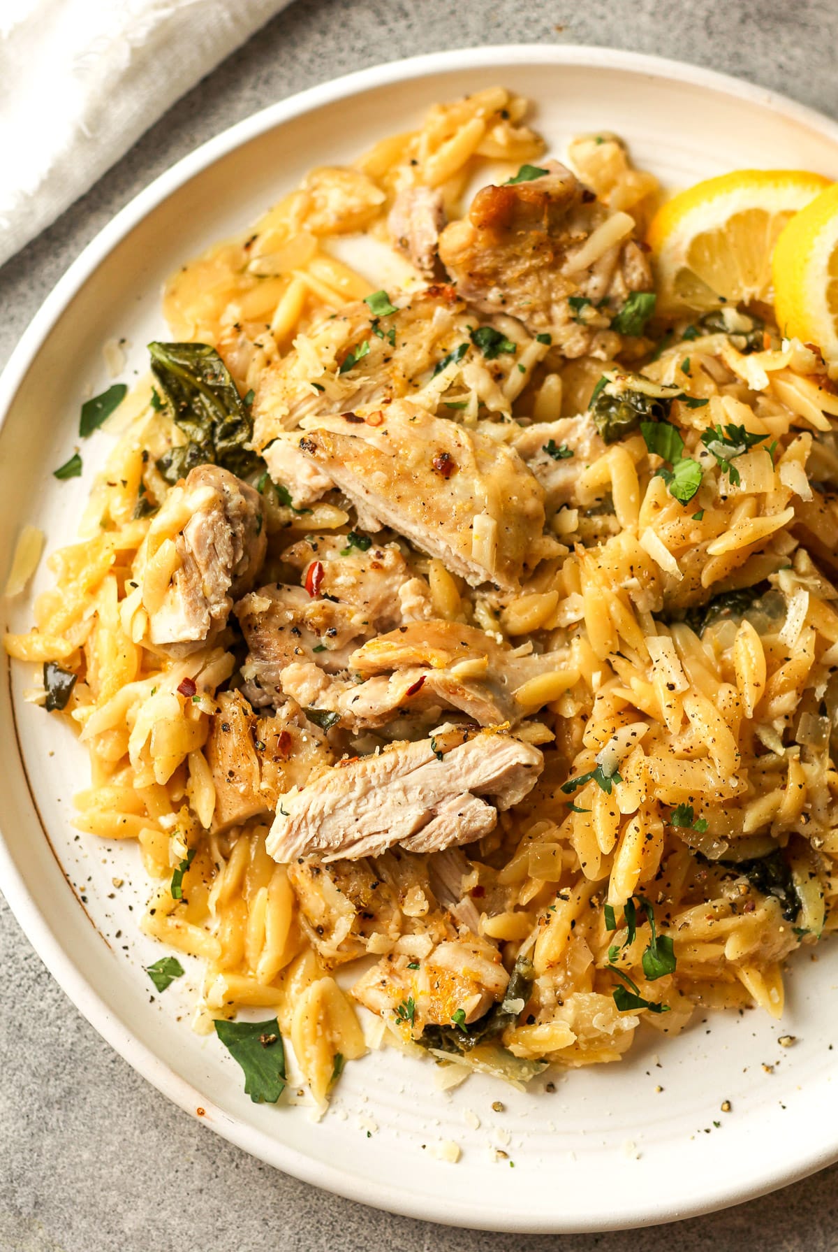 A white plate of the pasta bake with sliced chicken and lemons slices.