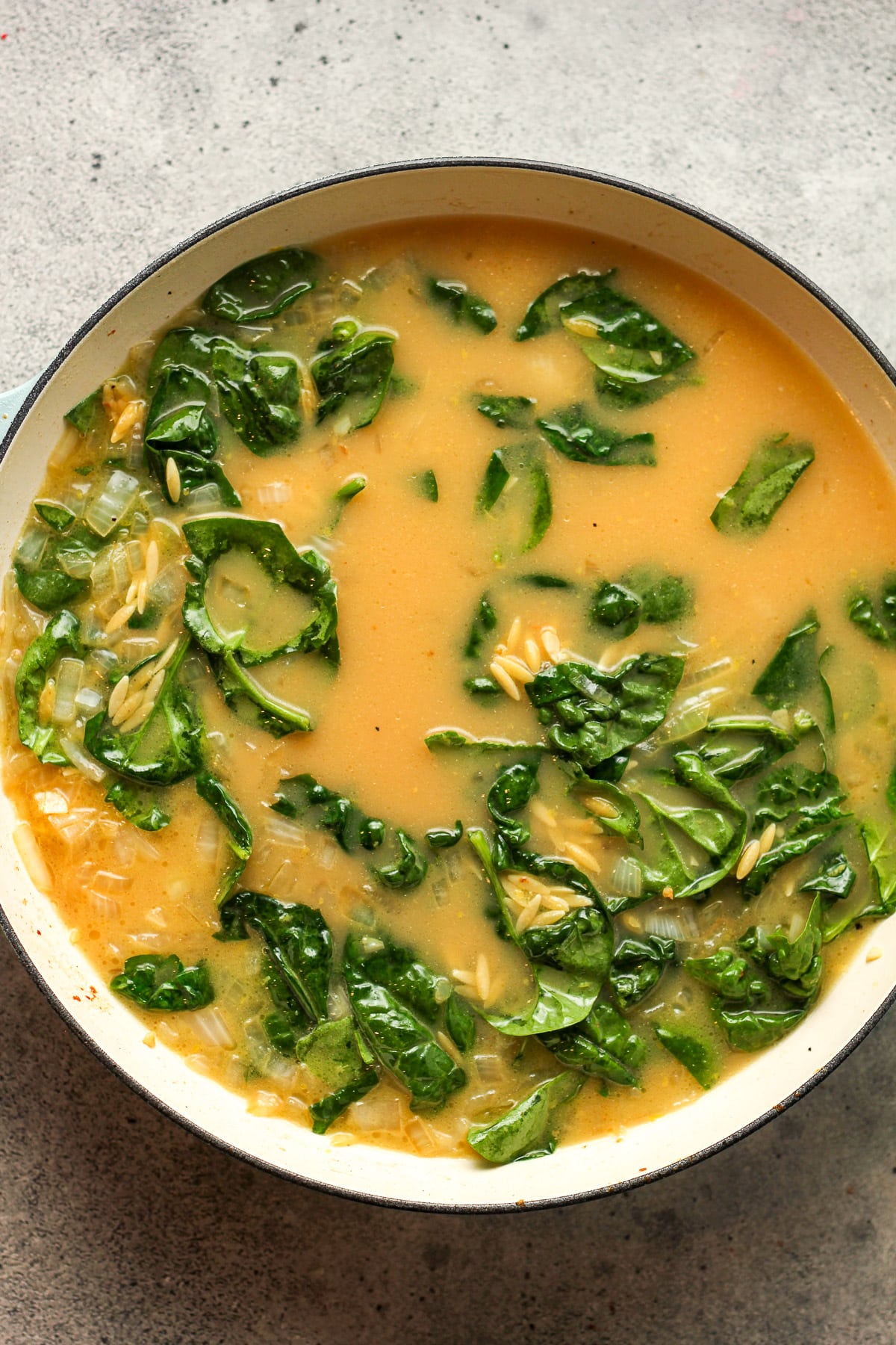 A skillet of the veggies, liquids, orzo, and spinach.