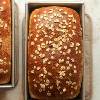 Two loaves of oatmeal bread with oats on top.