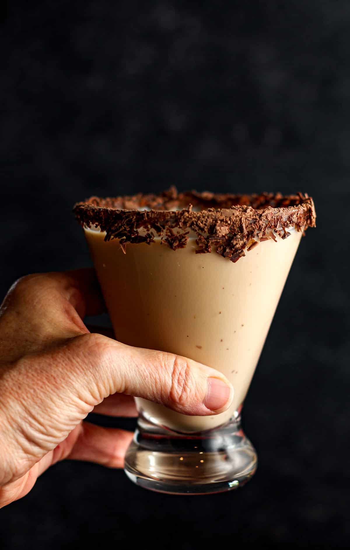 Side view of a hand holding a chocolate martini with chocolate shavings.