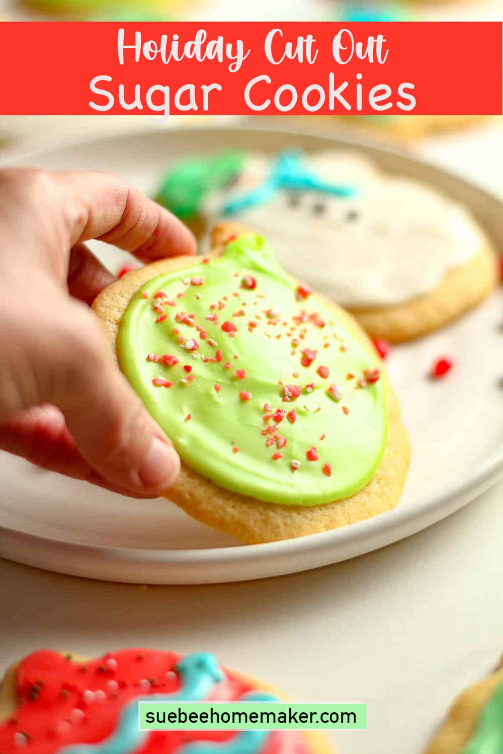 Side view of a hand lifting an ornament cookie off a plate.