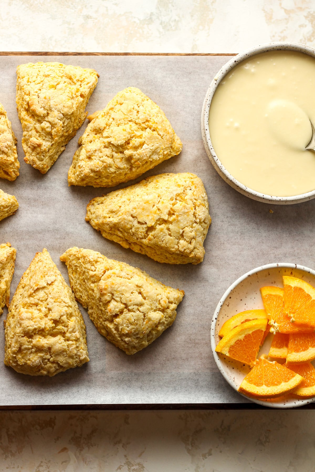 A board of orange scones with a bowl of glaze.