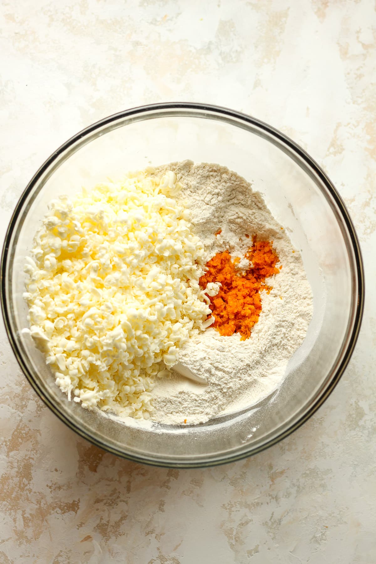 A bowl of the dry ingredients plus orange zest plus frozen butter.