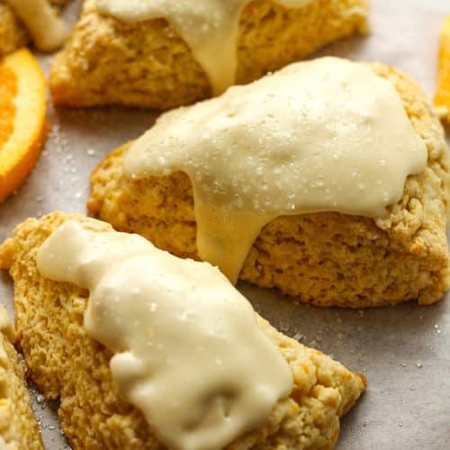 Side view of some glazed orange scones with orange slices.