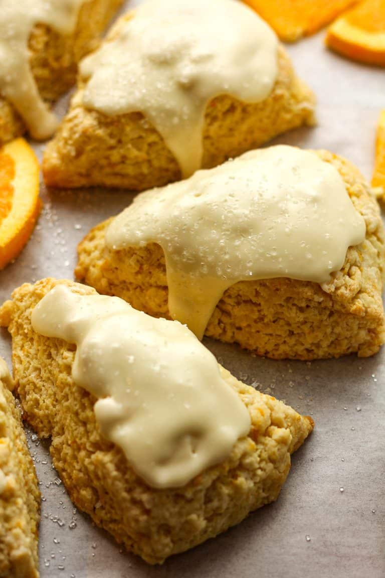 Side view of some glazed orange scones with orange slices.