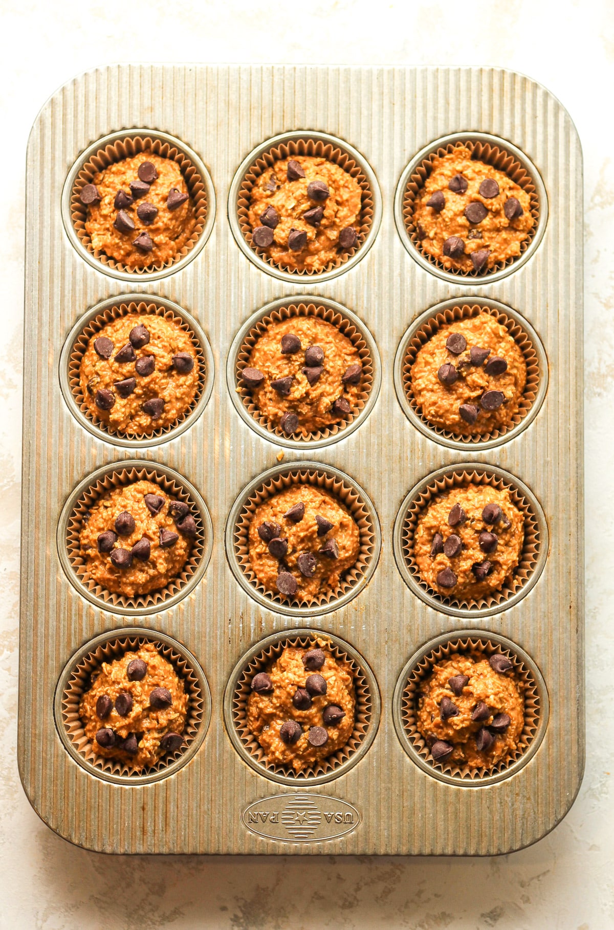 A 12-cup muffin tin with liners filled with pumpkin batter.