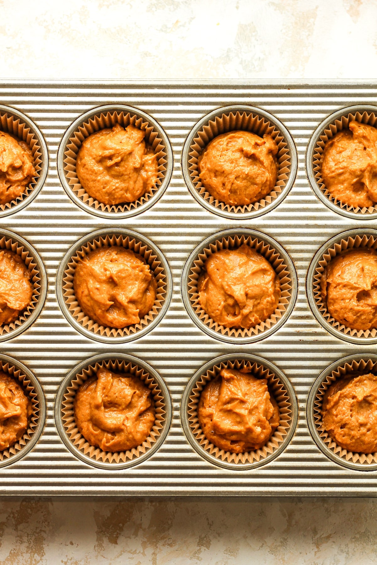 A muffin tin of the liners with pumpkin batter.