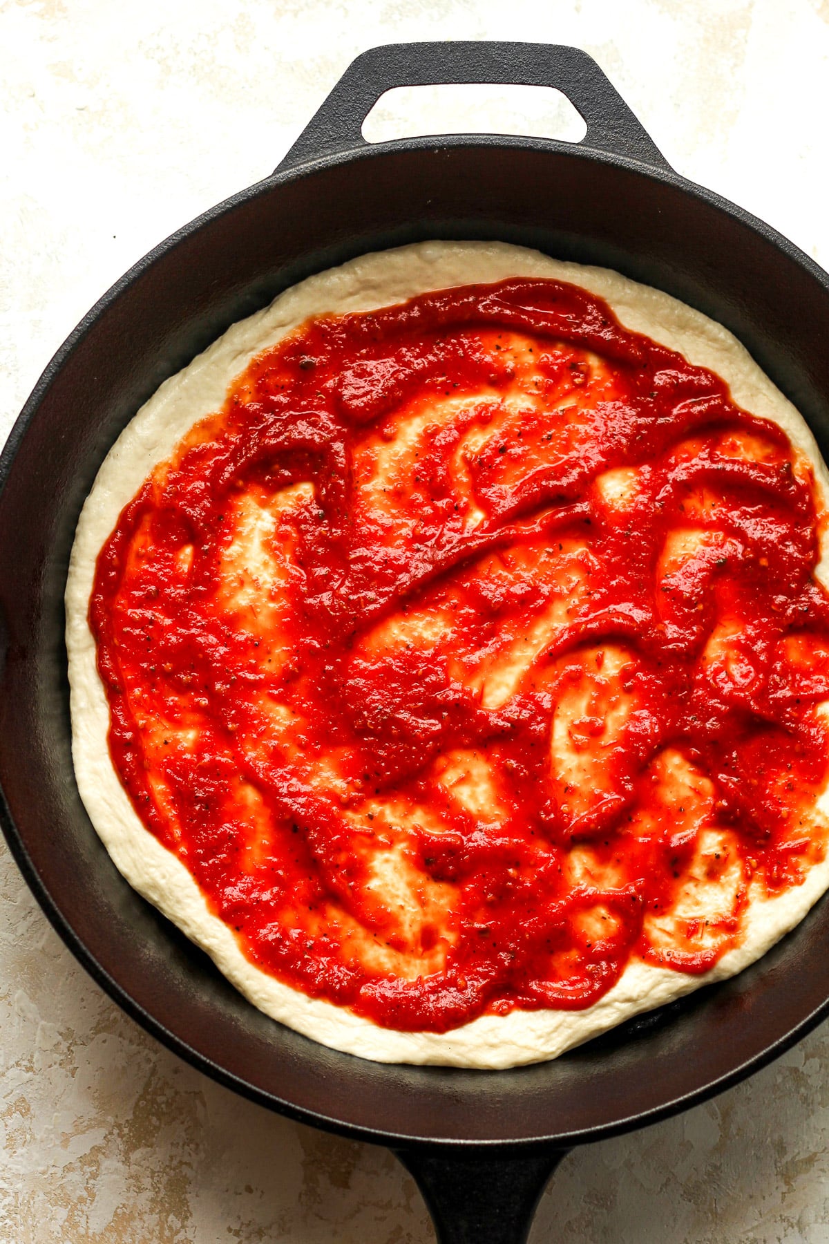 A skillet of the pizza dough with pizza sauce on top.