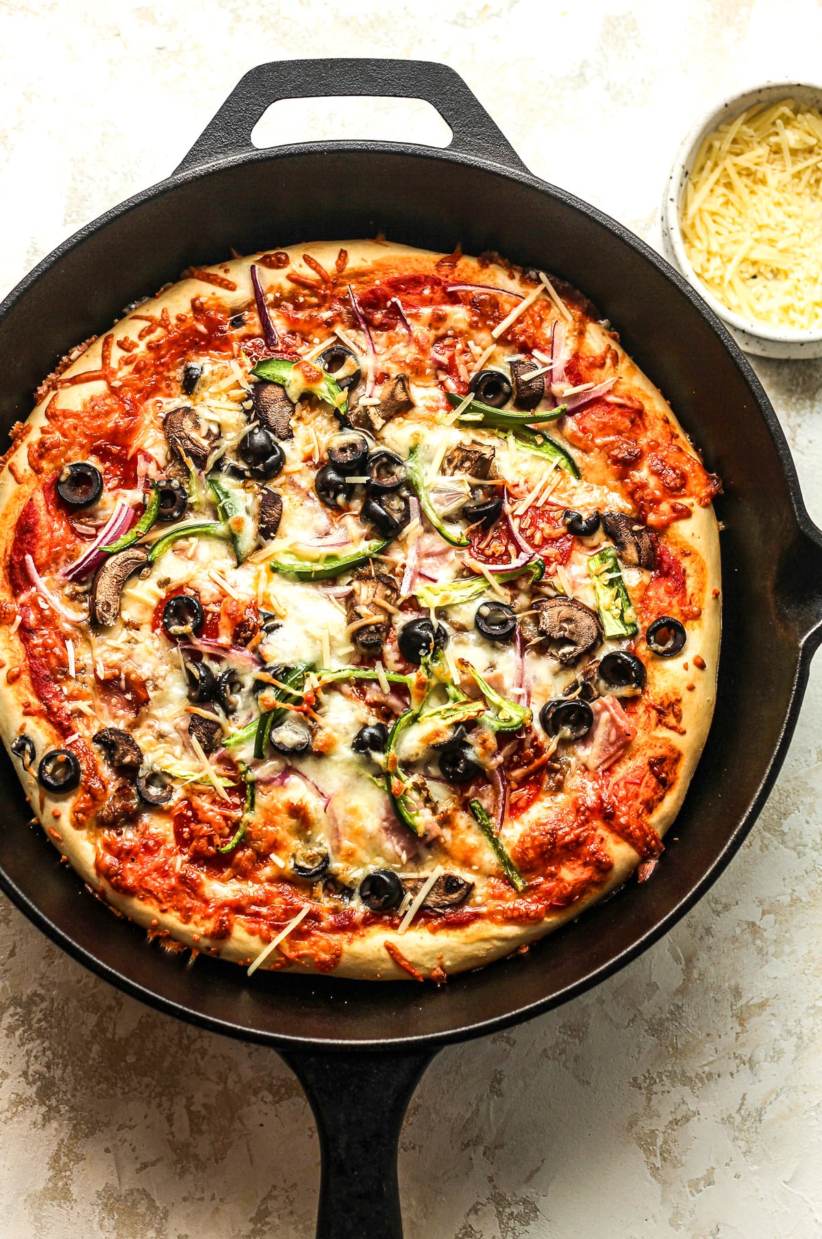 A cast iron skillet with a just baked Supreme pizza.