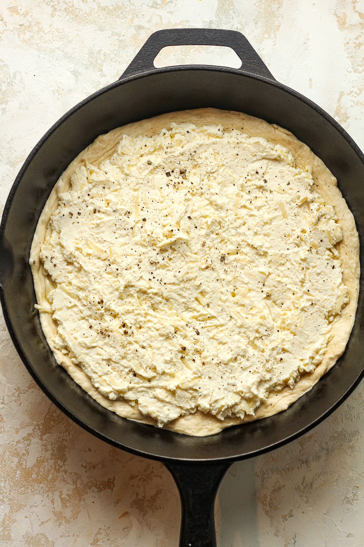 A skillet with the pizza dough with the cheese spread on top.