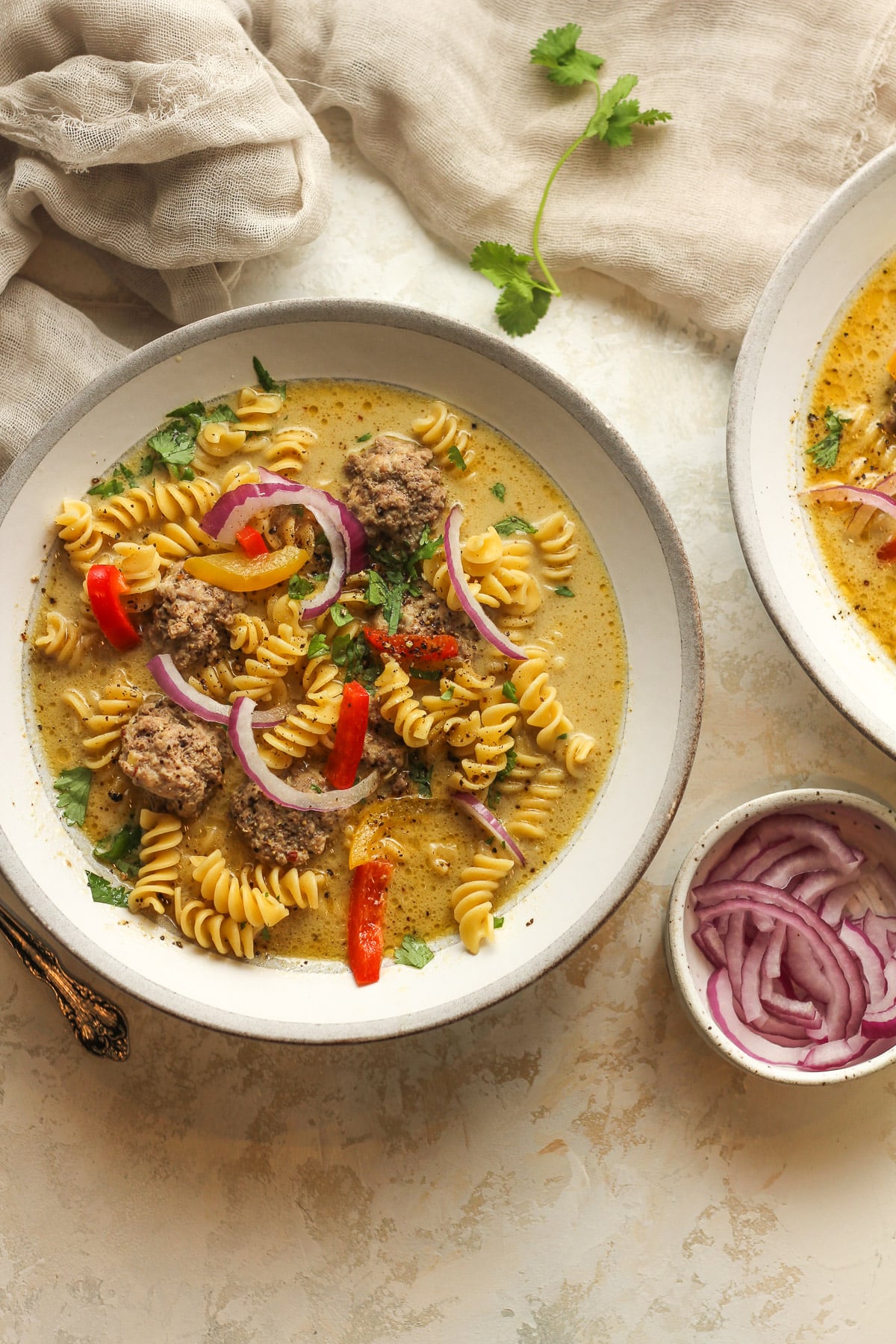 Two bowls of Thai meatball soup with a small bowl of sliced red onion.