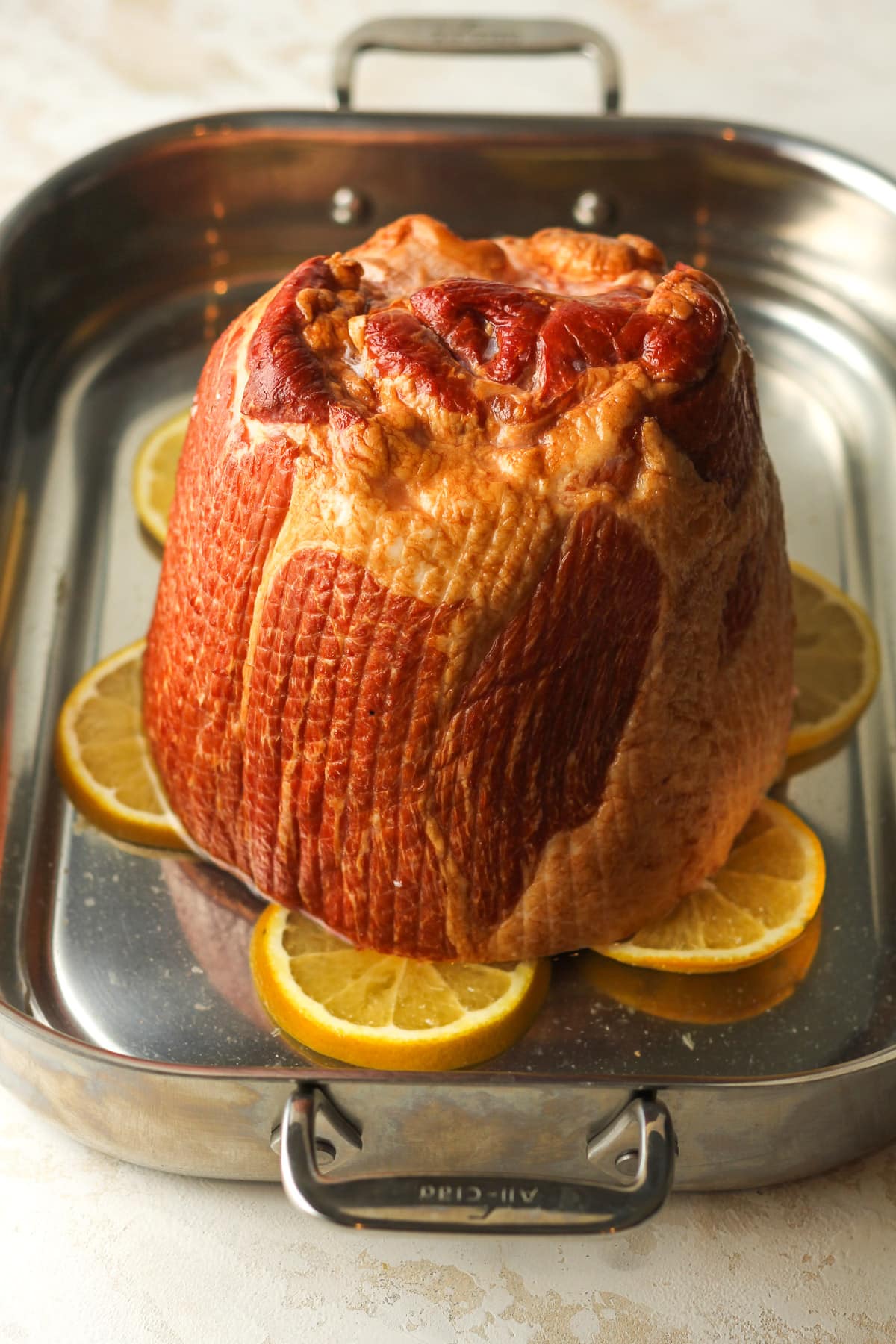 A pan with a bone in ham on orange slices with water.