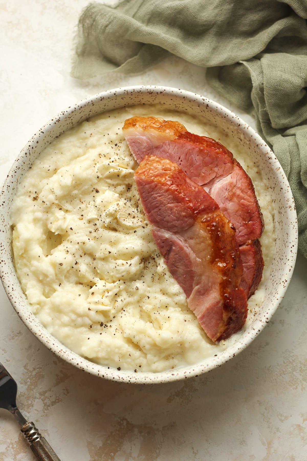 A bowl of mashed potatoes and two slices of ham on top.