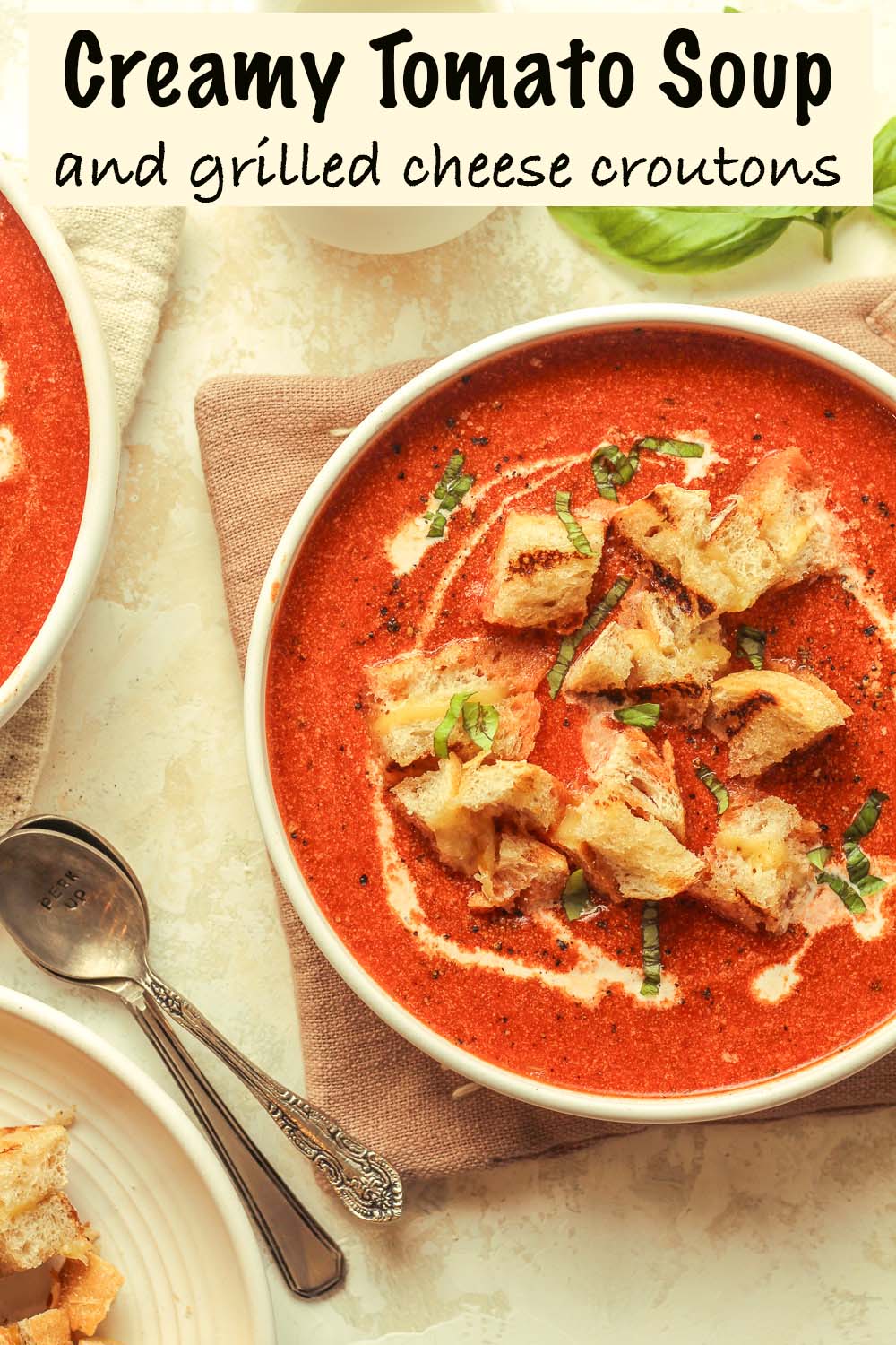 Two bowls of creamy tomato soup and grilled cheese croutons.