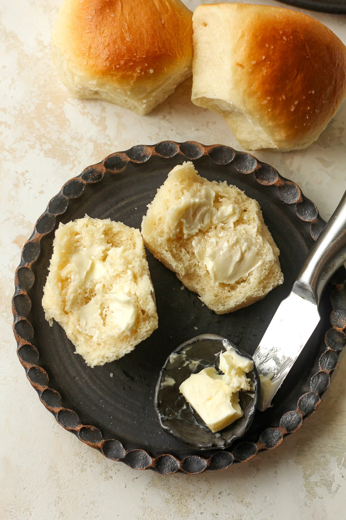 Overhead view of a small black plate with a buttered dinner roll.