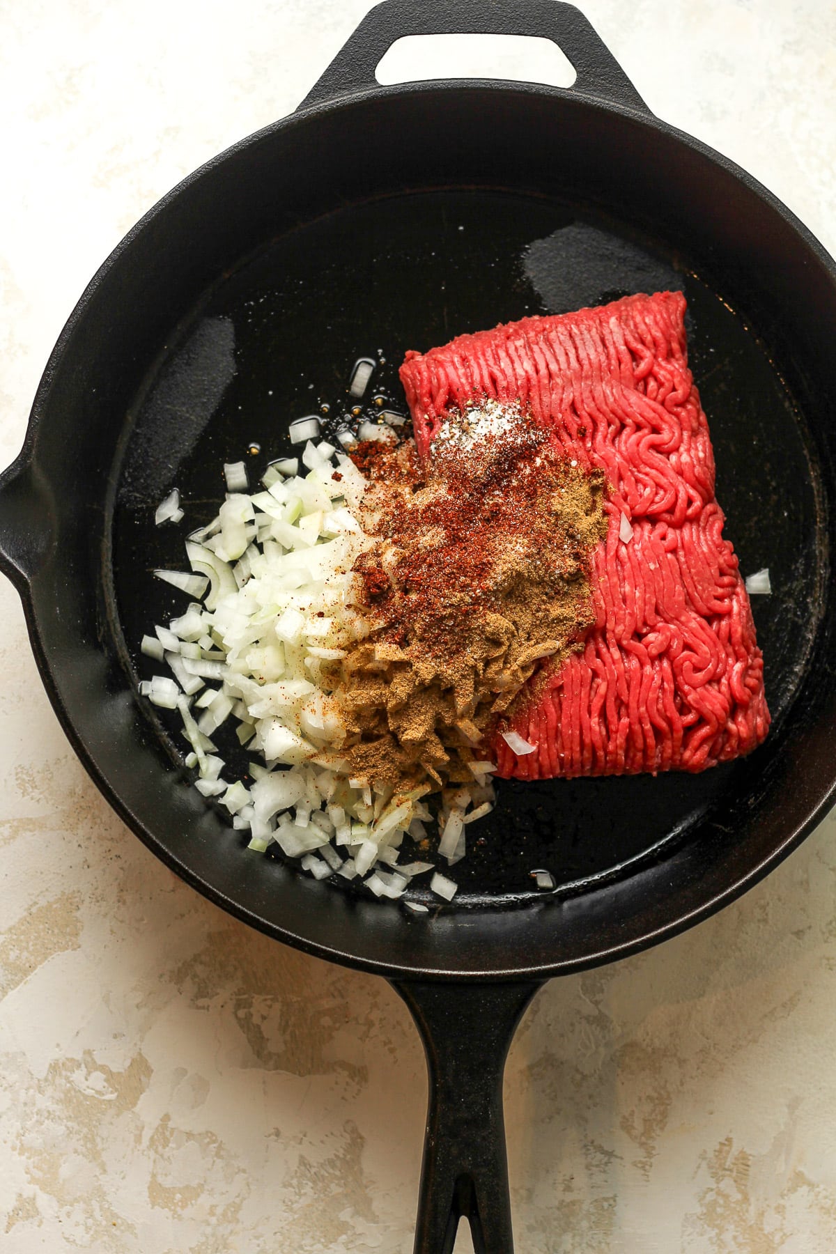 A skillet of the raw beef plus onions and seasoning.