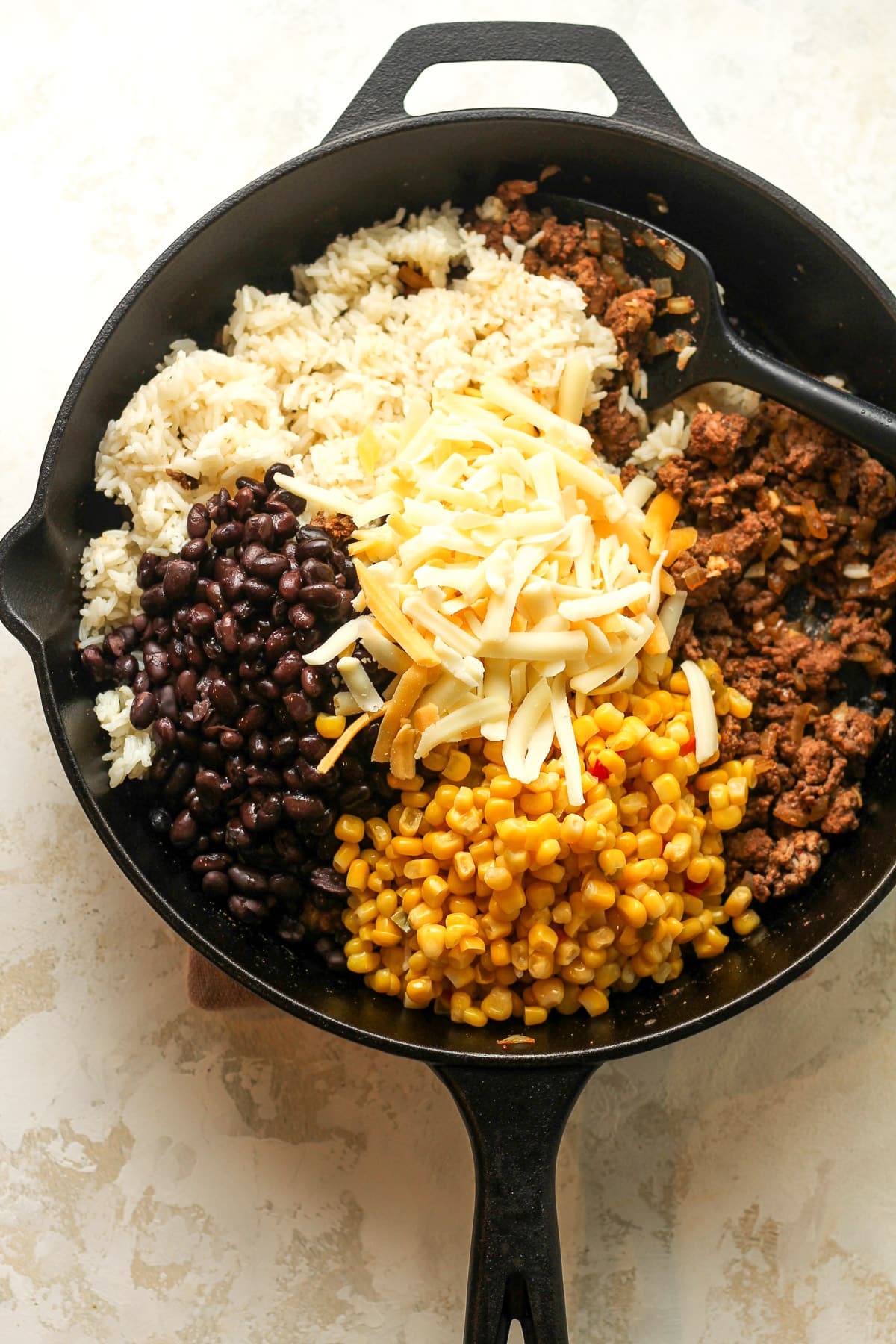 A skillet of the round meat topped with the beans, corn, rice, and cheese.