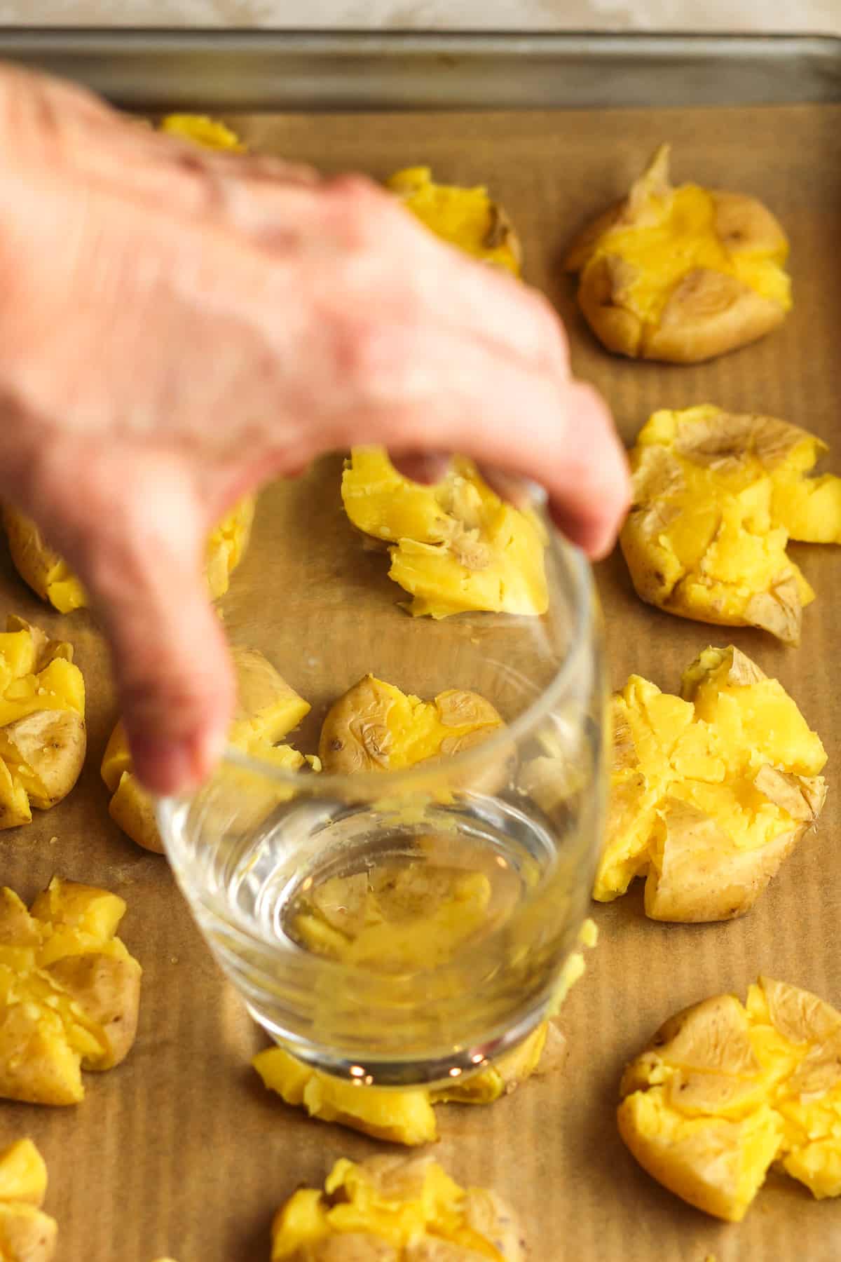 A hand pressing a glass on the yellow potatoes.