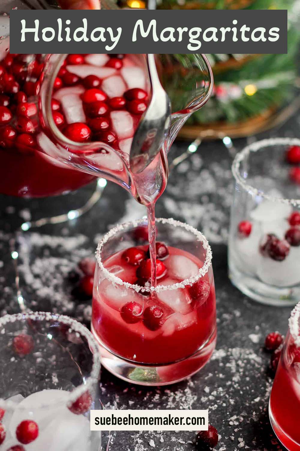 A pitcher of holiday margaritas pouring into a glass with cranberries.