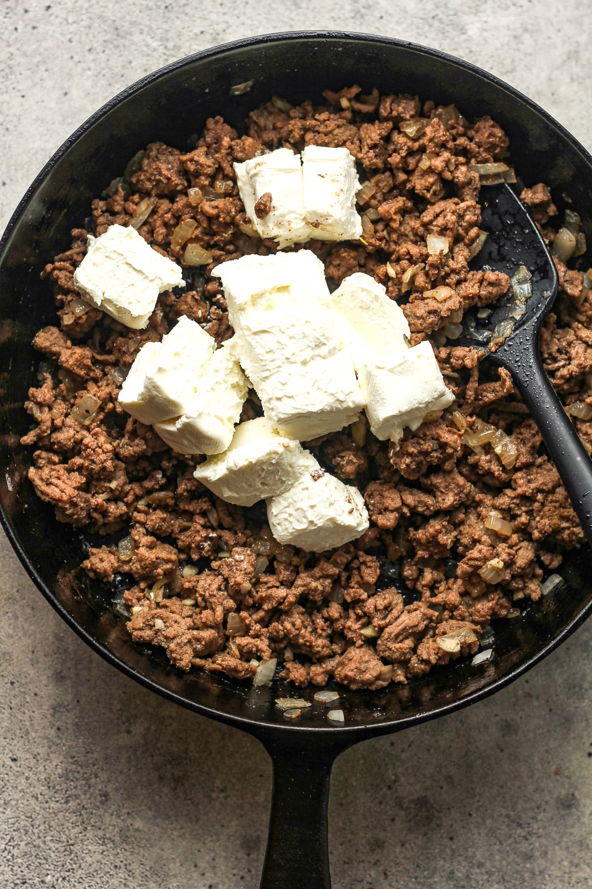 A skillet of the ground beef plus chunks of cream cheese.